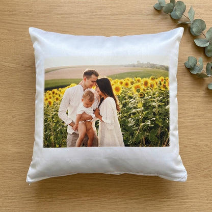 White pillow with a printed photo of a family in a sunflower field on a wooden surface.